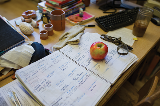 An educators desk with notebooks, books, an apple, and iced coffee.